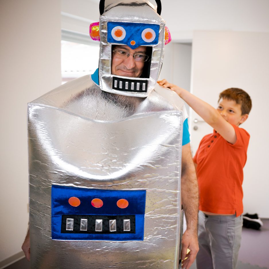 Roboter Kinderspiel - ein Kind versucht einen Roboter durch den Raum zu navigieren. Der Roboter ist ein umgekleideter Kursleiter